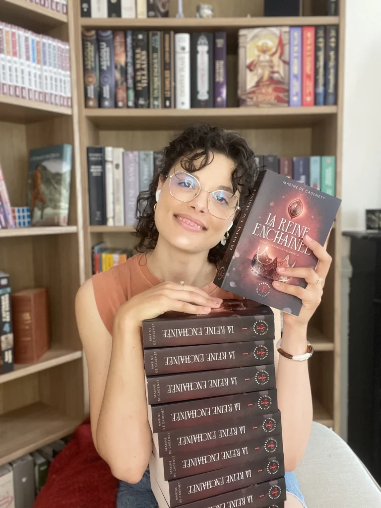 Photo de Marine de Cadenet, autrice de fantasy, avec ses exemplaires du tome 1 de La Reine enchaînée : Le Paria et l'Égorgeur.